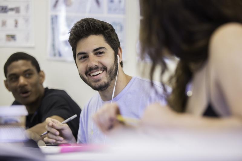 Student holds pen 和 smiles at another student while a third student looks on